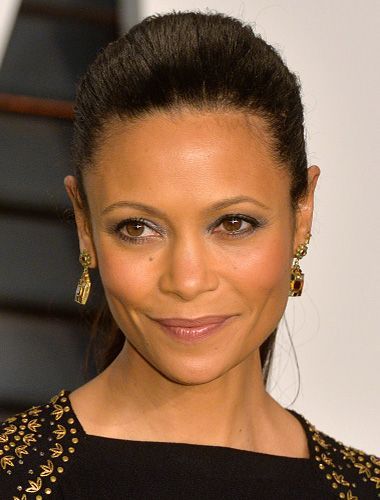 Woman with dark hair pulled back, wearing earrings and a black top with gold embellishments.