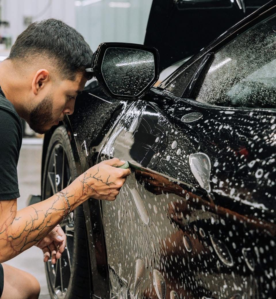 A man is cleaning the hood of a car in a garage.