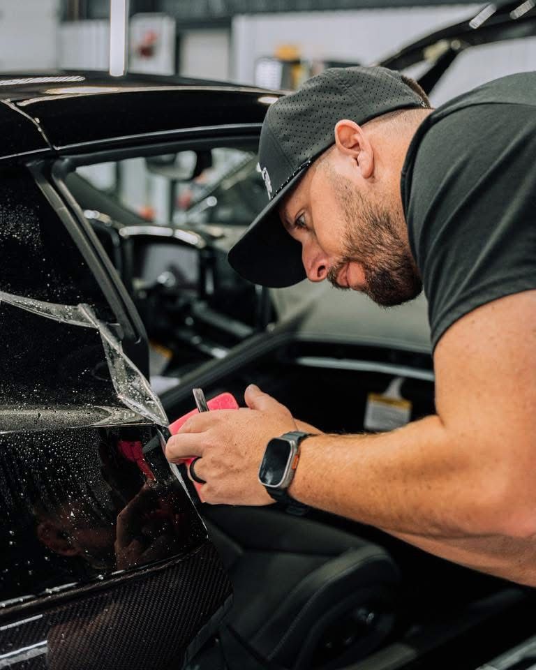 Technician polishing a black car panel with a cloth in a workshop