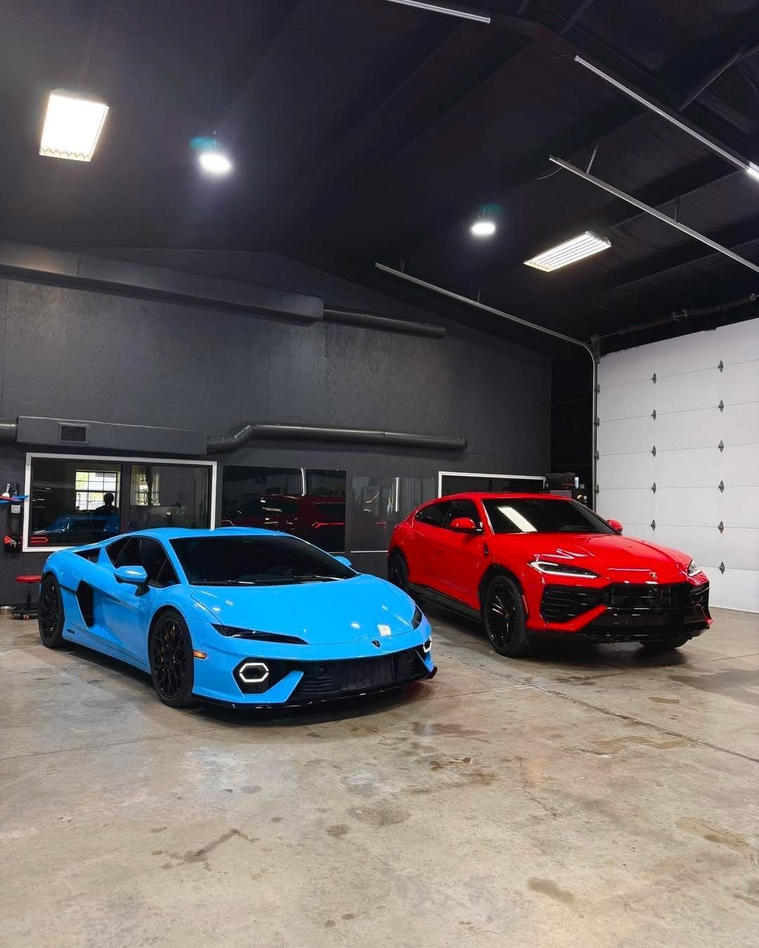 Blue and red sports cars parked inside a garage under bright overhead lights