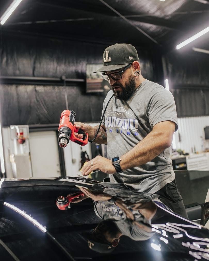 Detailer polishing a black car hood with a red buffer in a workshop