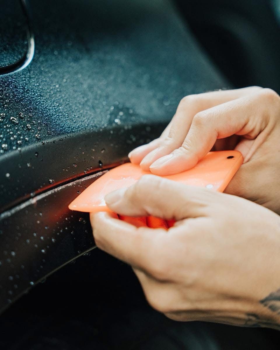 A man is applying a protective film to the front of a white car.