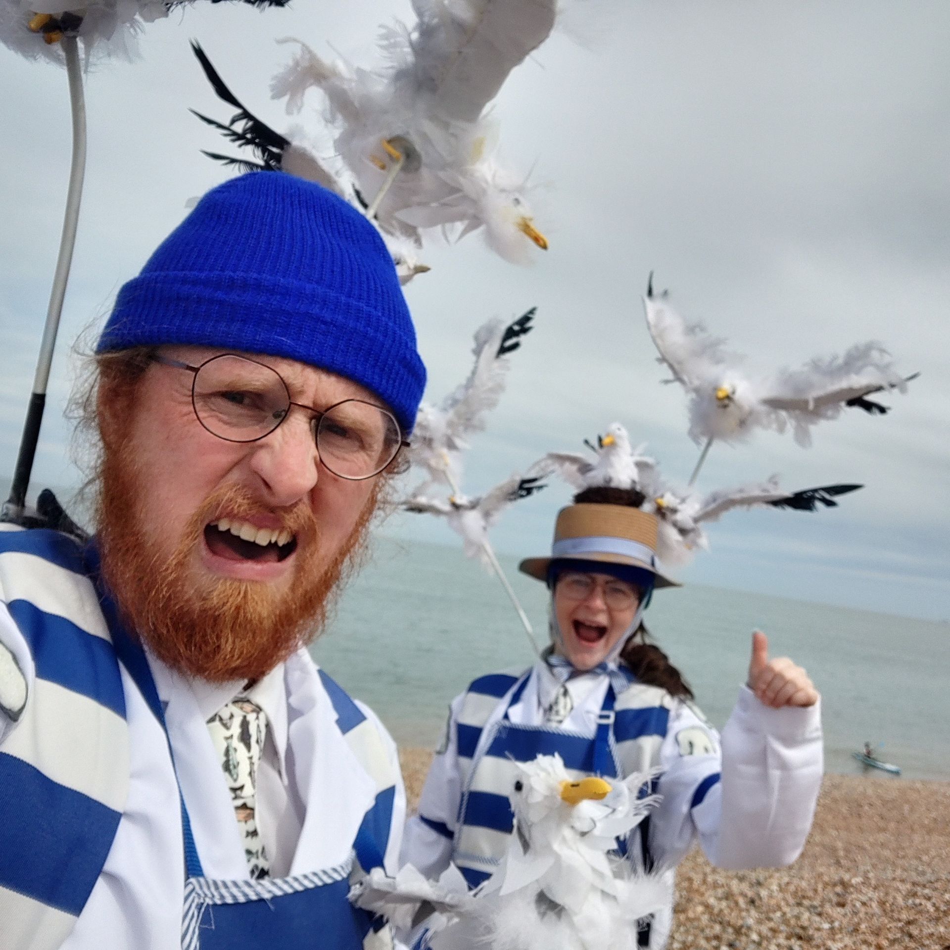 Two performers dressed as fishmongers stand looking concerned as seagull puppets circle above their head