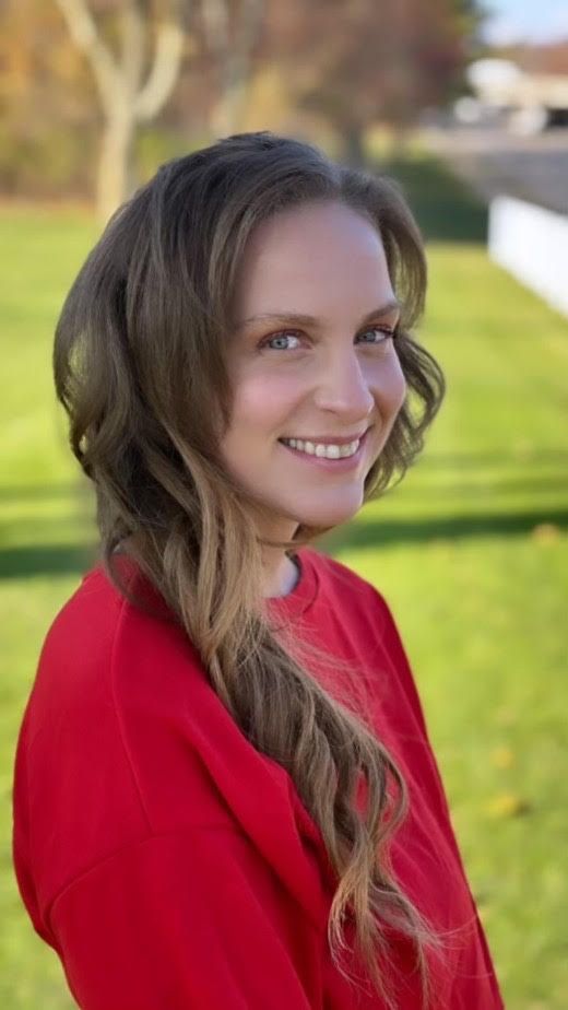 Smiling person in a red top outdoors with a blurred green lawn background