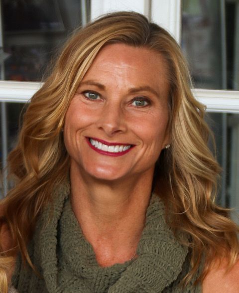 Smiling woman with wavy blonde hair wearing a green knit top, standing outdoors.