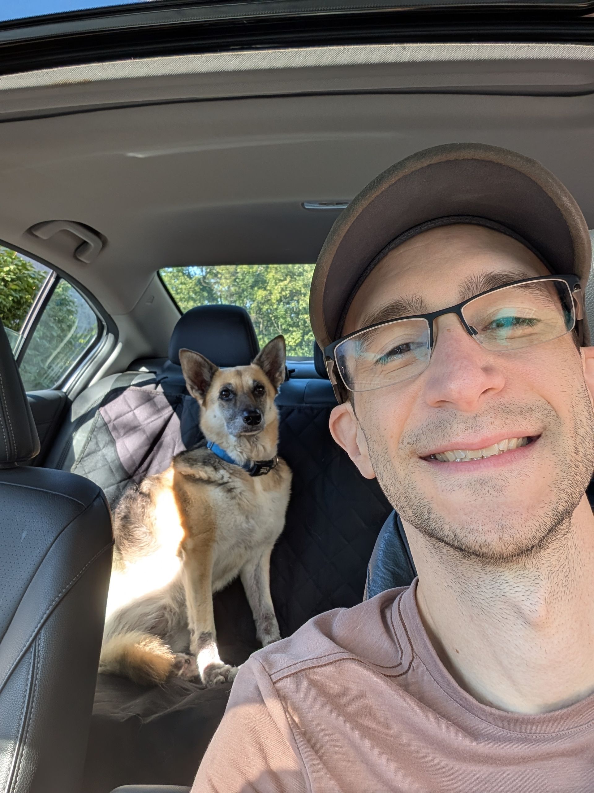 Man and dog sitting in a car, both facing the camera and smiling