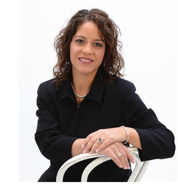 Woman seated on a white chair against a white background, smiling with hands folded over the backrest