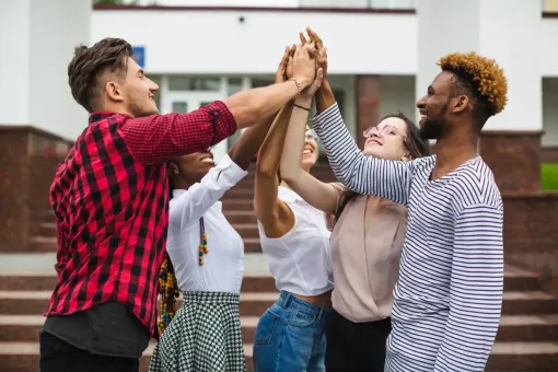 Five friends outdoors high-fiving with hands raised, smiling and celebrating together.