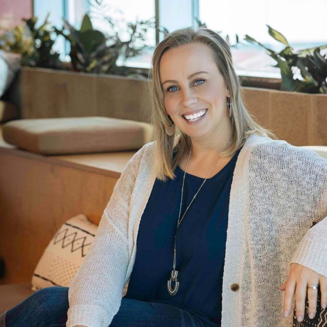 Smiling woman in a navy top and cream cardigan seated in a modern lounge chair