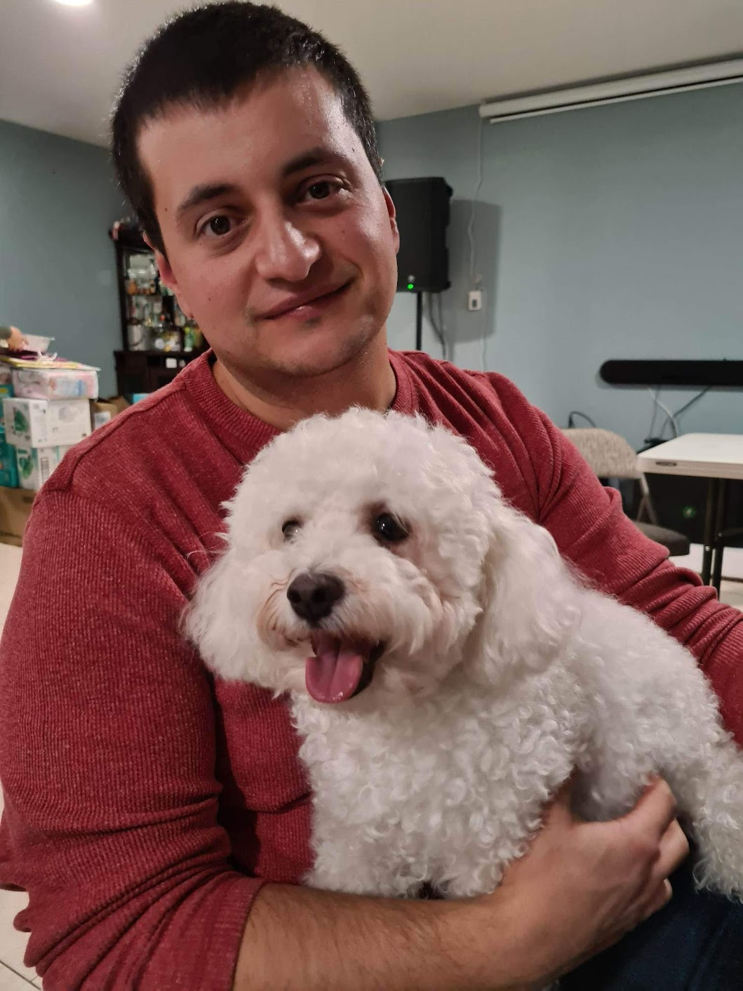 Person holding a fluffy white dog indoors, both looking at the camera.