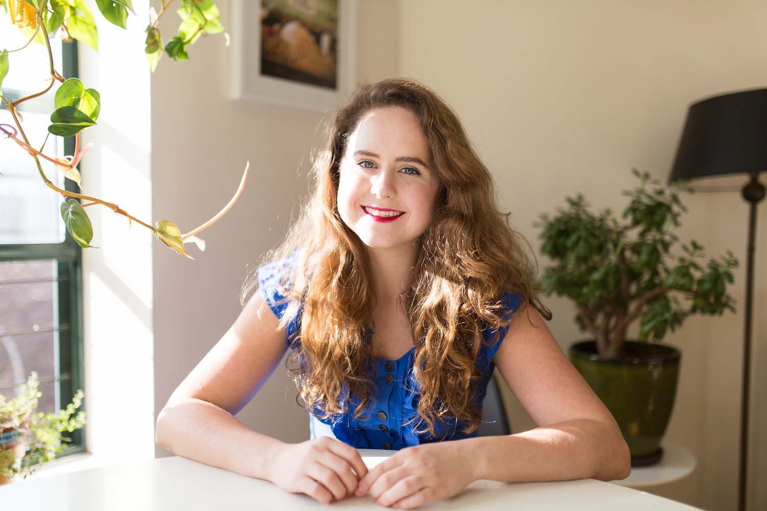 Woman with long dark hair wearing a floral top, smiling in a softly lit indoor setting