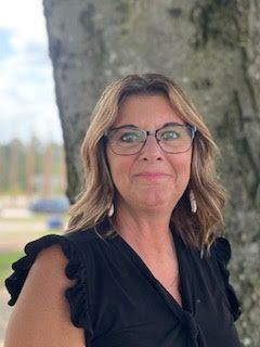 Smiling woman in glasses and black top standing beside a stone pillar outdoors
