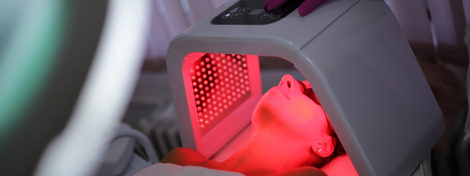 Person undergoing red light therapy facial treatment. Red light emanating from device on face.