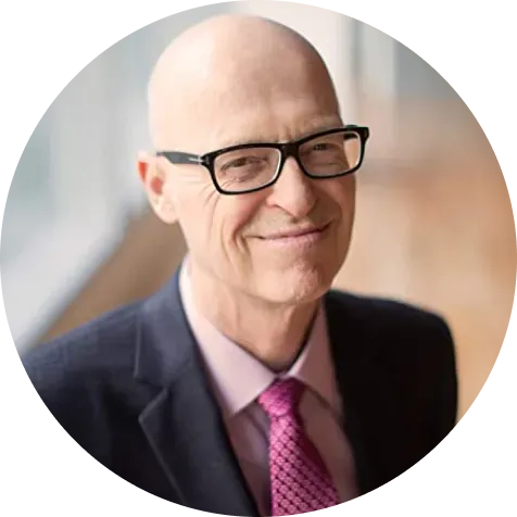 Bald man with glasses in suit and tie smiles.