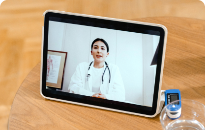Doctor on a tablet screen during a video consultation beside a digital thermometer on a wooden table
