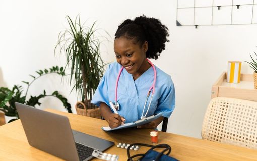 Woman working on a laptop and tablet at a desk with a coffee mug and houseplants.
