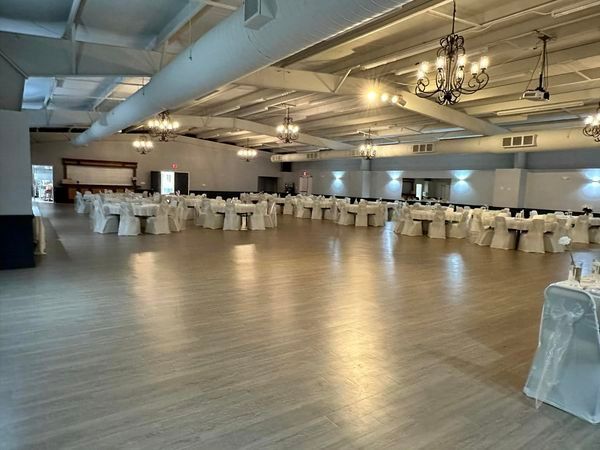 Empty banquet hall with white tablecloth-covered tables, chandeliers, and wood-look flooring