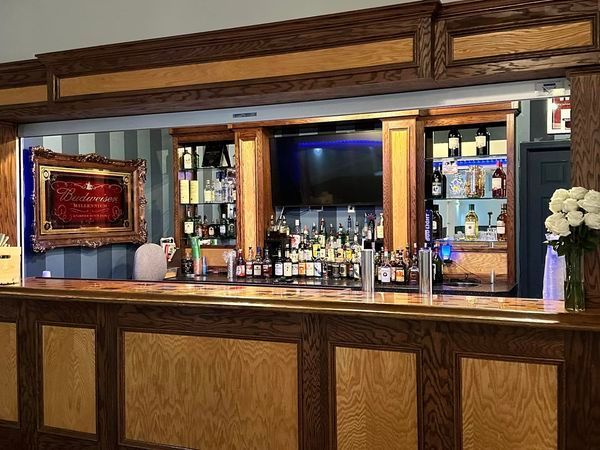 Hotel bar with wood-paneled counter, shelves of bottles, and a TV above the back bar