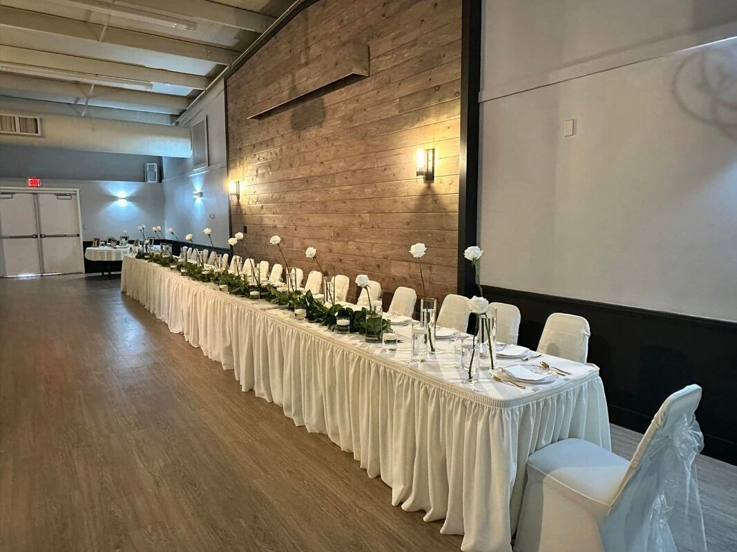 Long banquet table with white chairs set along a brick-walled event hall