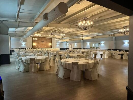 Empty banquet hall with round, white-clothed tables and chandeliers on a polished wood floor
