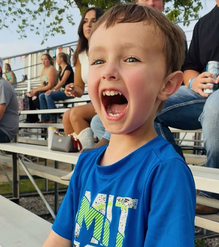 Smiling child in a blue shirt cheering in bleachers outdoors