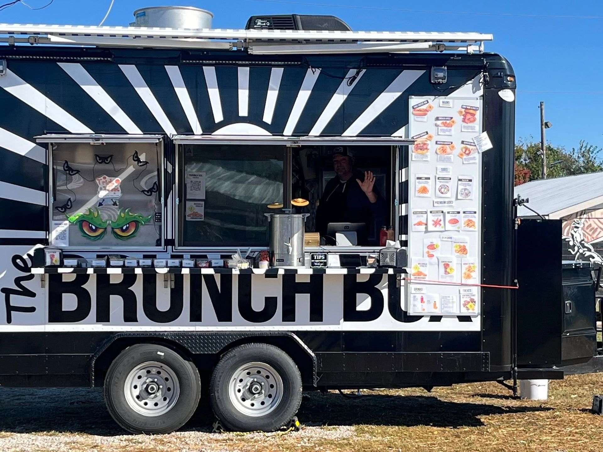 Black brunch food truck with striped awning and menu board, serving customers outdoors.