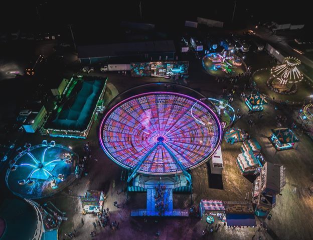 Night aerial view of a colorful carnival with a giant illuminated Ferris wheel and glowing rides