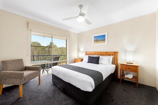 A hotel room with a king size bed , chair , nightstand and ceiling fan.