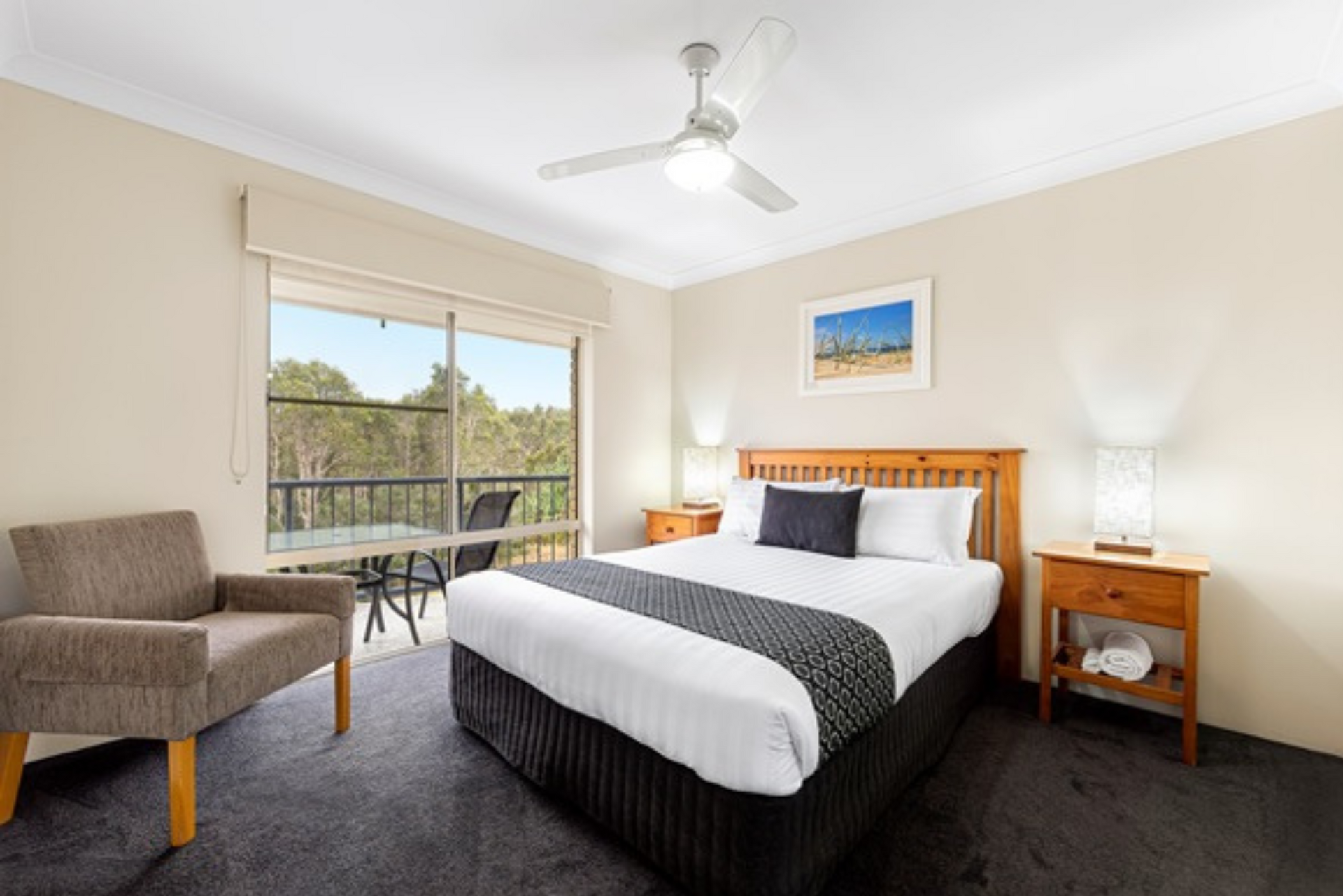 A hotel room with a king size bed , chair , nightstand and ceiling fan.