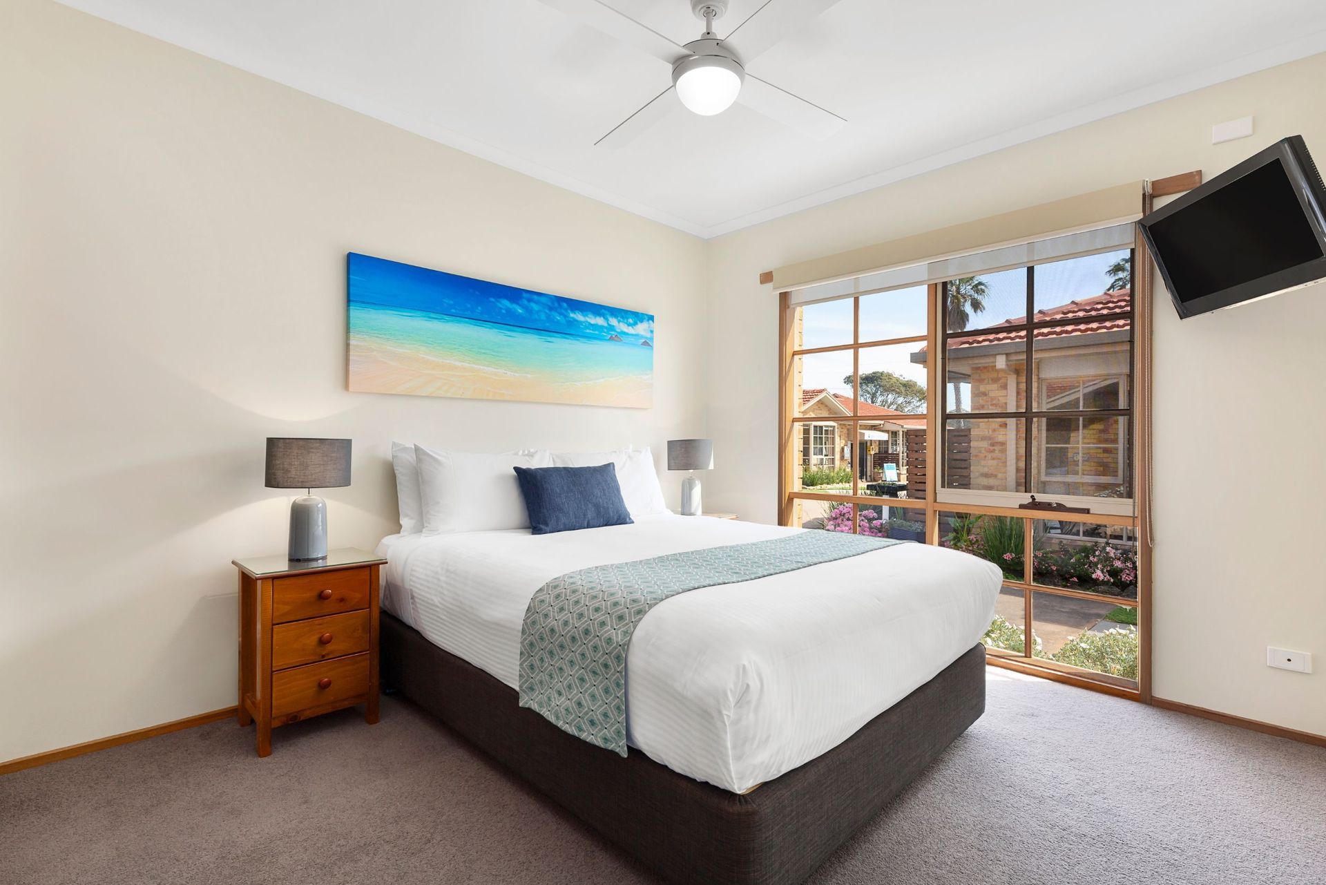 A bedroom with a king size bed , nightstand , television and ceiling fan.