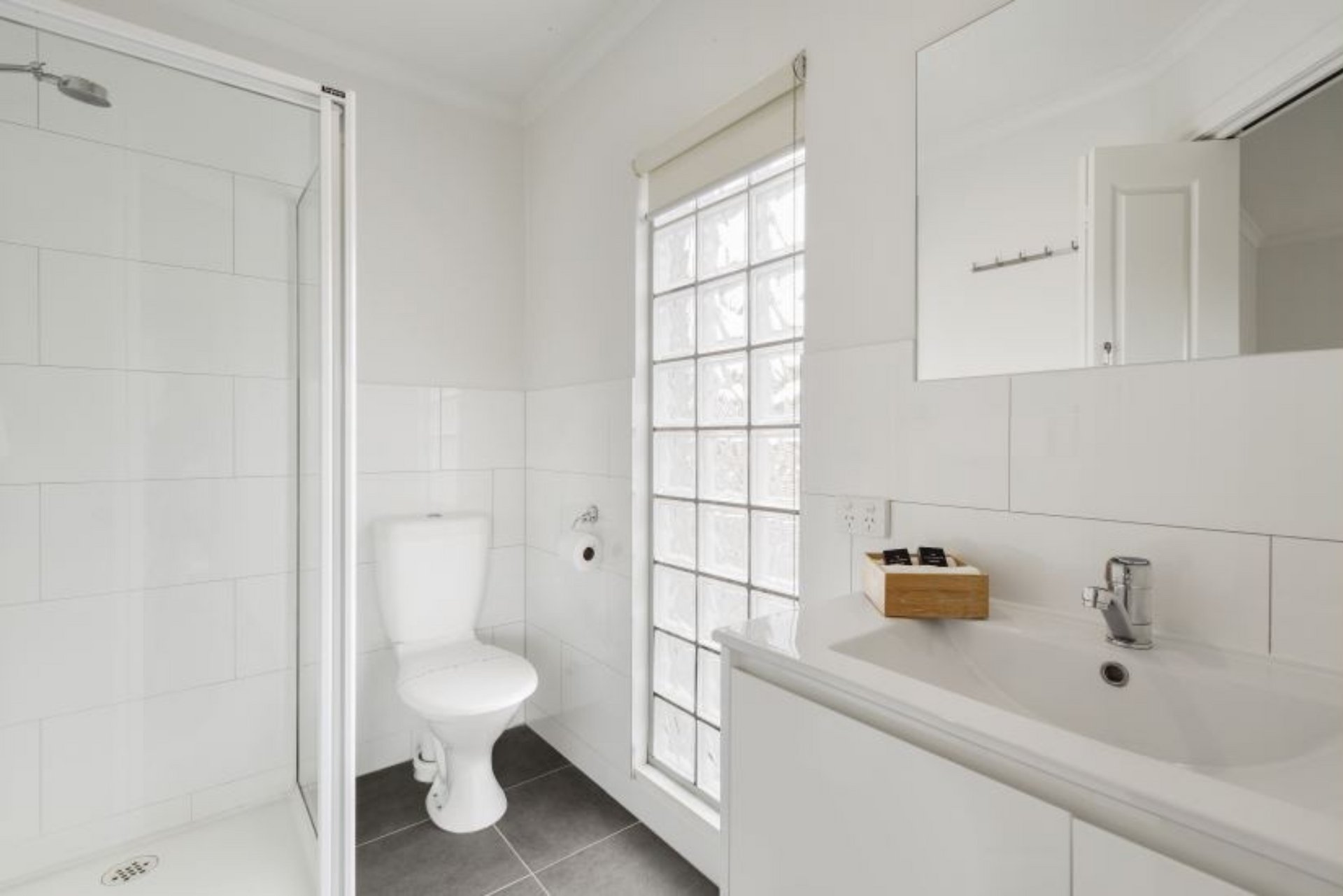 A bathroom with a toilet , sink , shower and mirror.