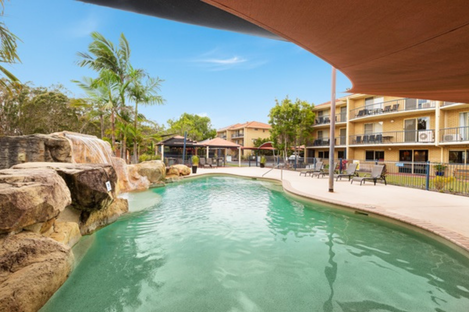 A large swimming pool with a waterfall in the middle of a resort.