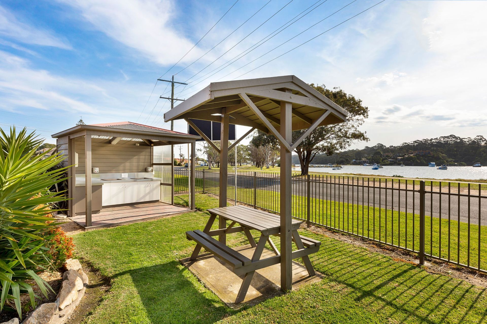 A picnic table with a shelter over it is in the grass next to a fence.