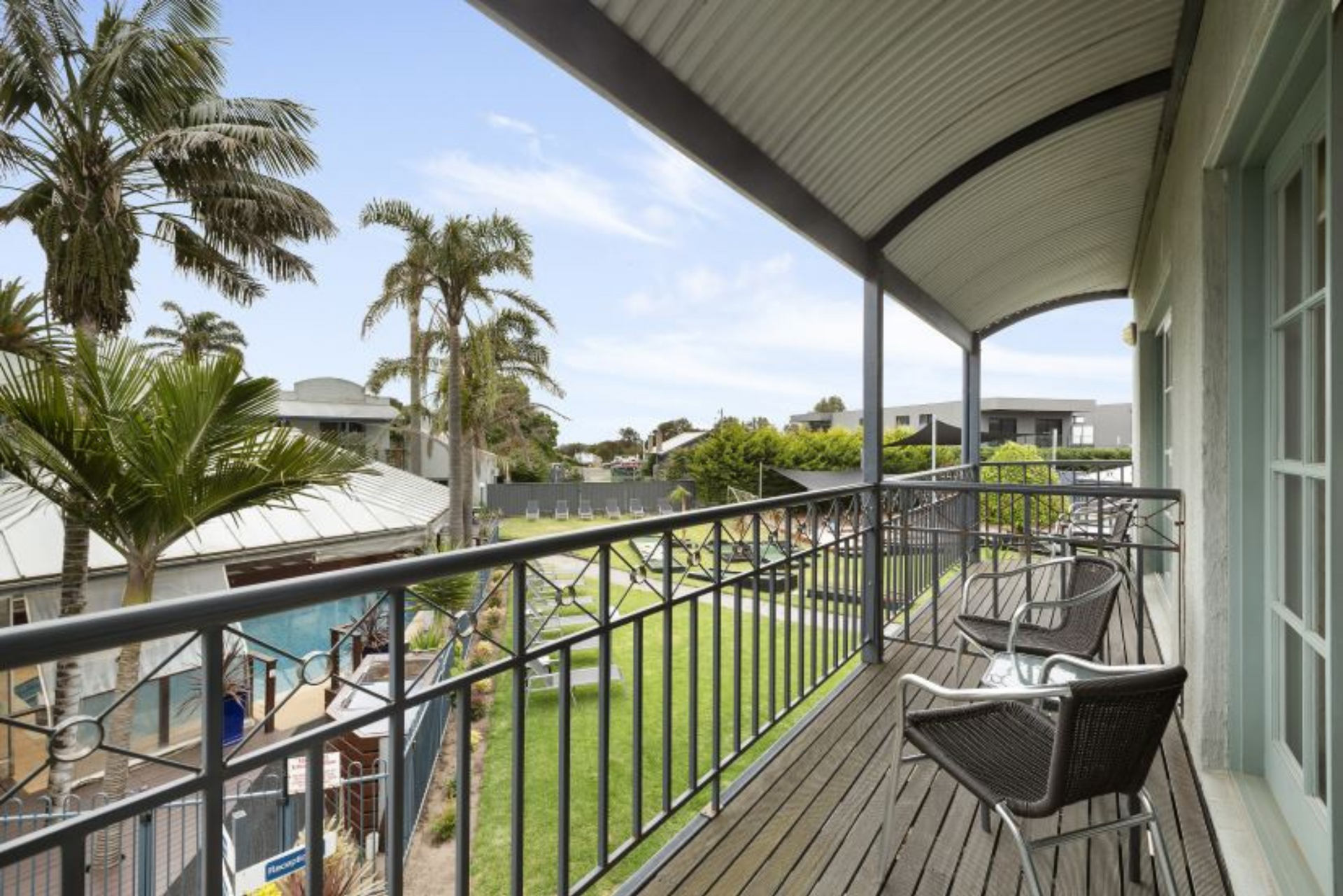 A balcony with chairs and a railing overlooking a lush green yard