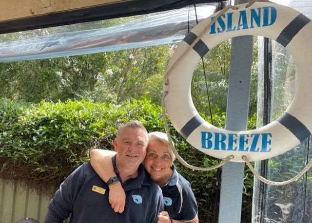 A man and woman are posing in front of a life preserver that says island breeze