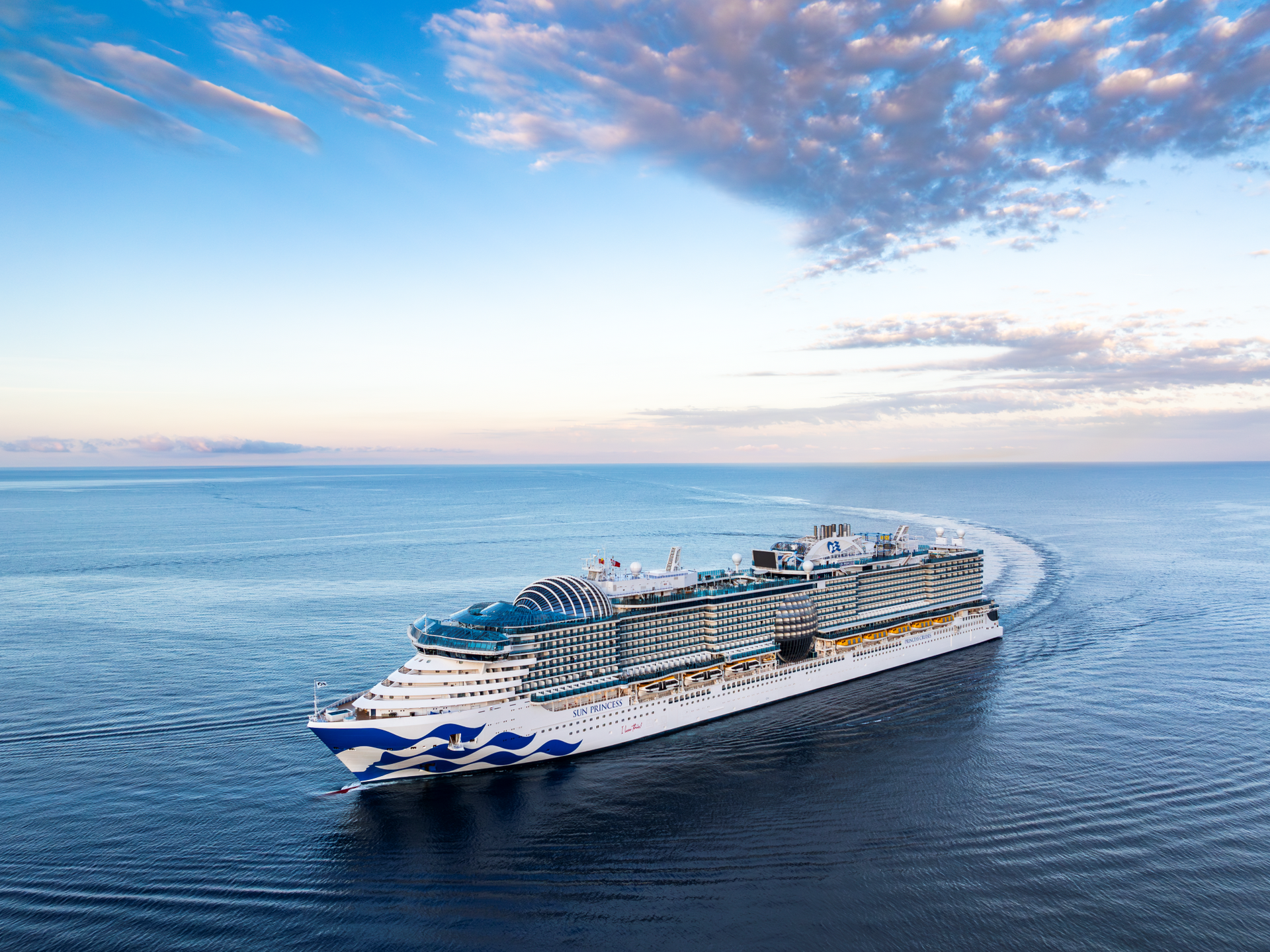 Sun Princess cruise ship sailing on a calm ocean under a partly cloudy sky.
