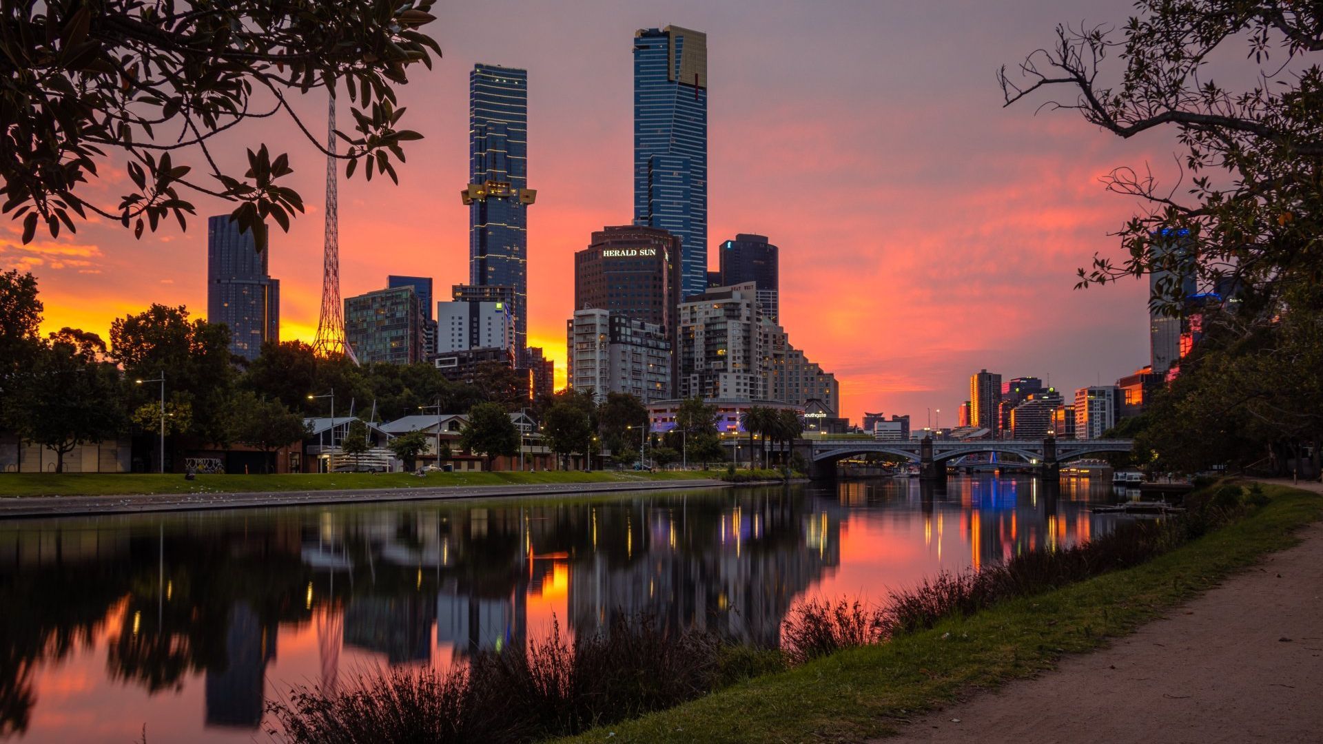 A city skyline is reflected in a body of water at sunset.