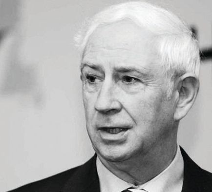 A black and white portrait of a person in a suit, looking slightly off-camera with a focused, serious expression.