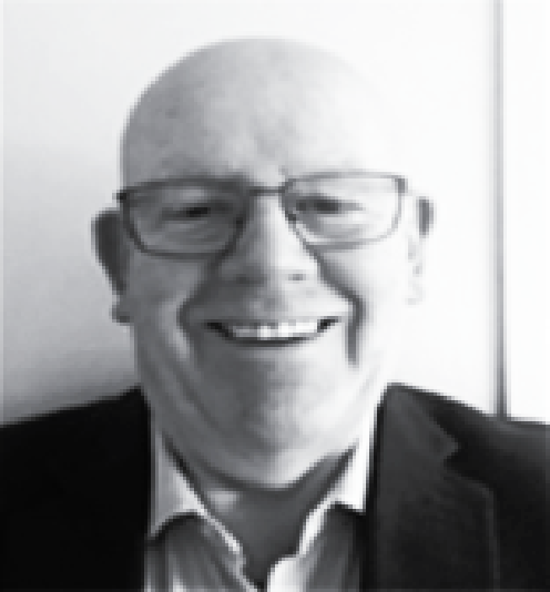A headshot of a smiling person with a shaved head, wearing glasses and a dark blazer over a collared shirt.