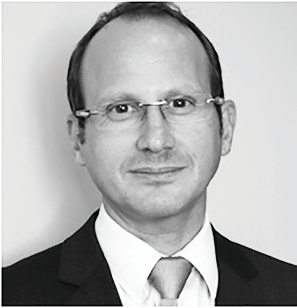 Headshot of a professional wearing glasses, a suit, and a tie against a plain light-colored background.