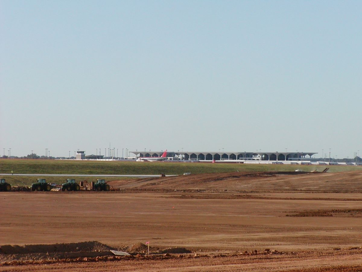 A plane is taking off from an airport runway with tractors in the foreground.