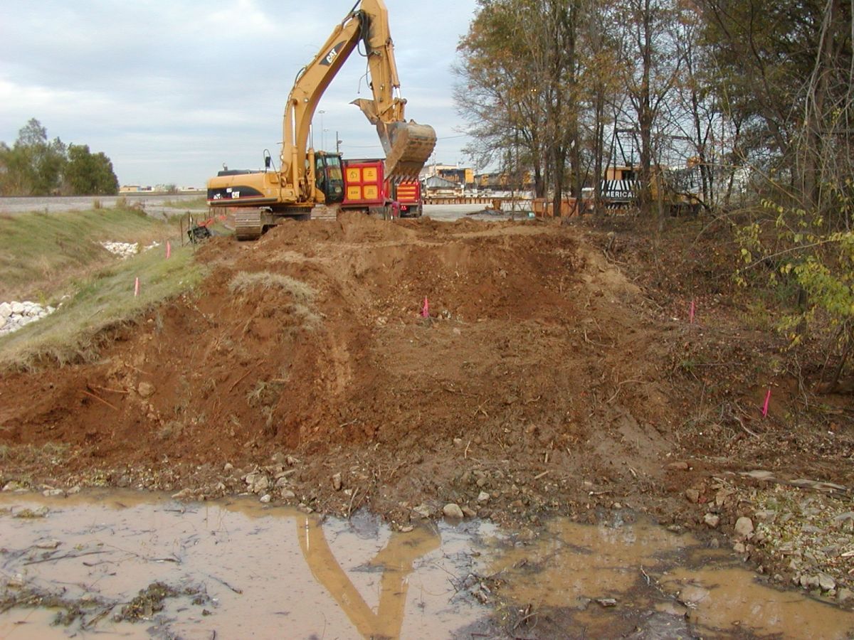 A large yellow excavator is digging a hole in the dirt
