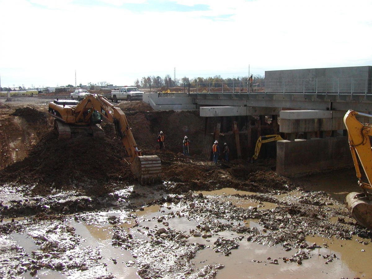 A construction site with a lot of mud and a yellow excavator in the foreground.