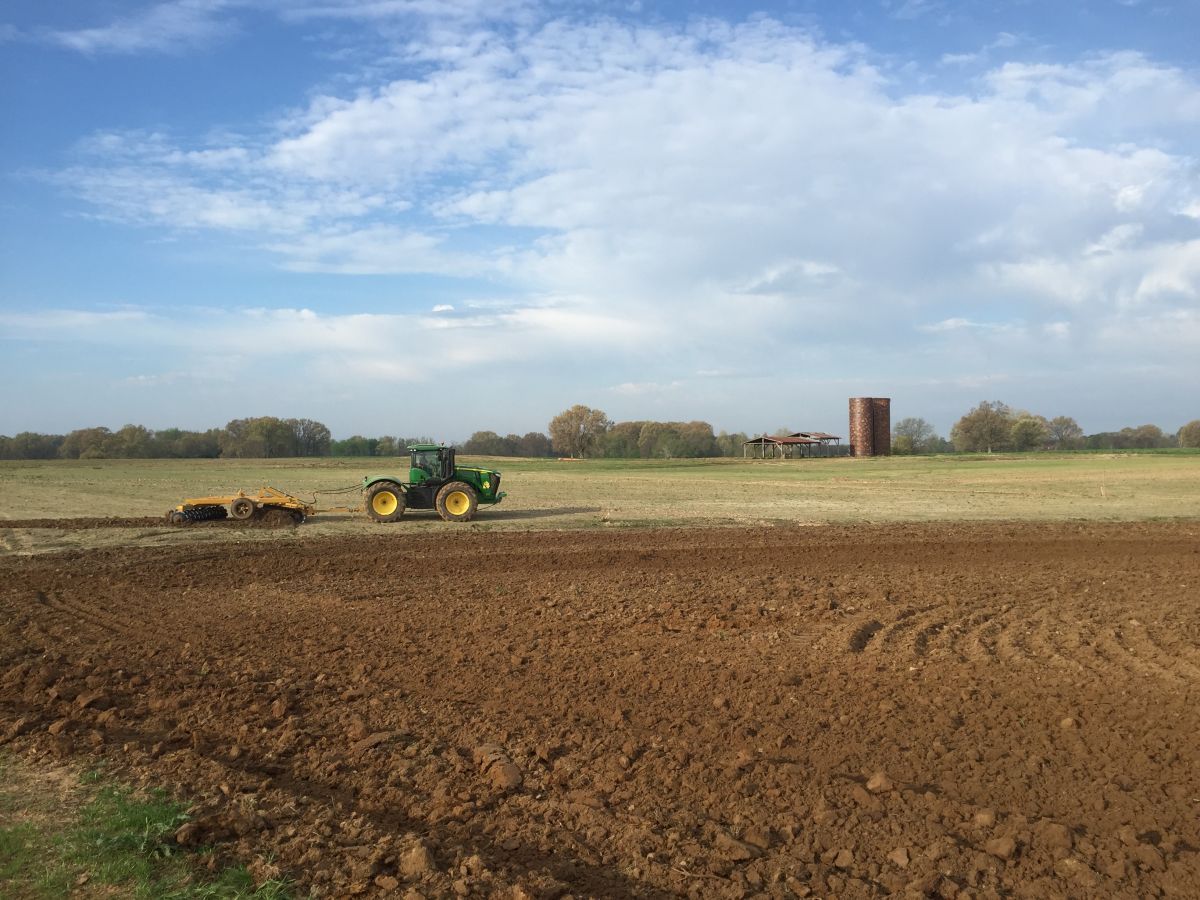 A tractor is plowing a field with a silo in the background.