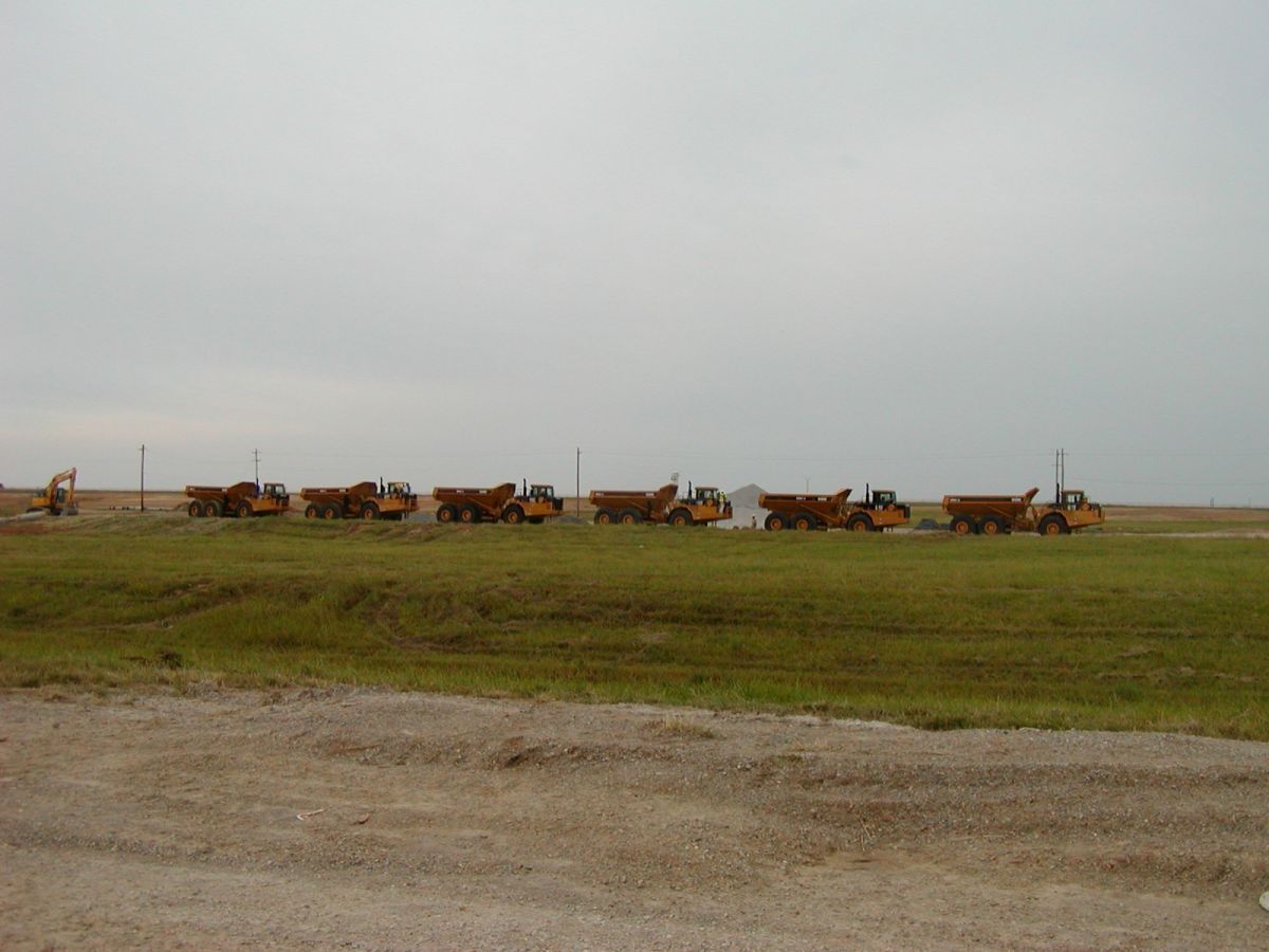 A row of dump trucks are parked in a grassy field