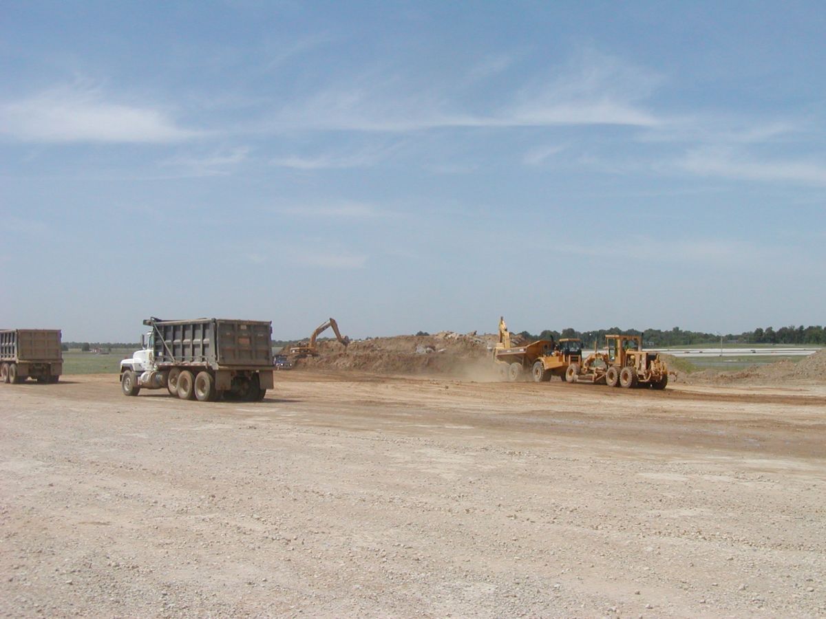 A dump truck is driving down a dirt road next to a bulldozer.