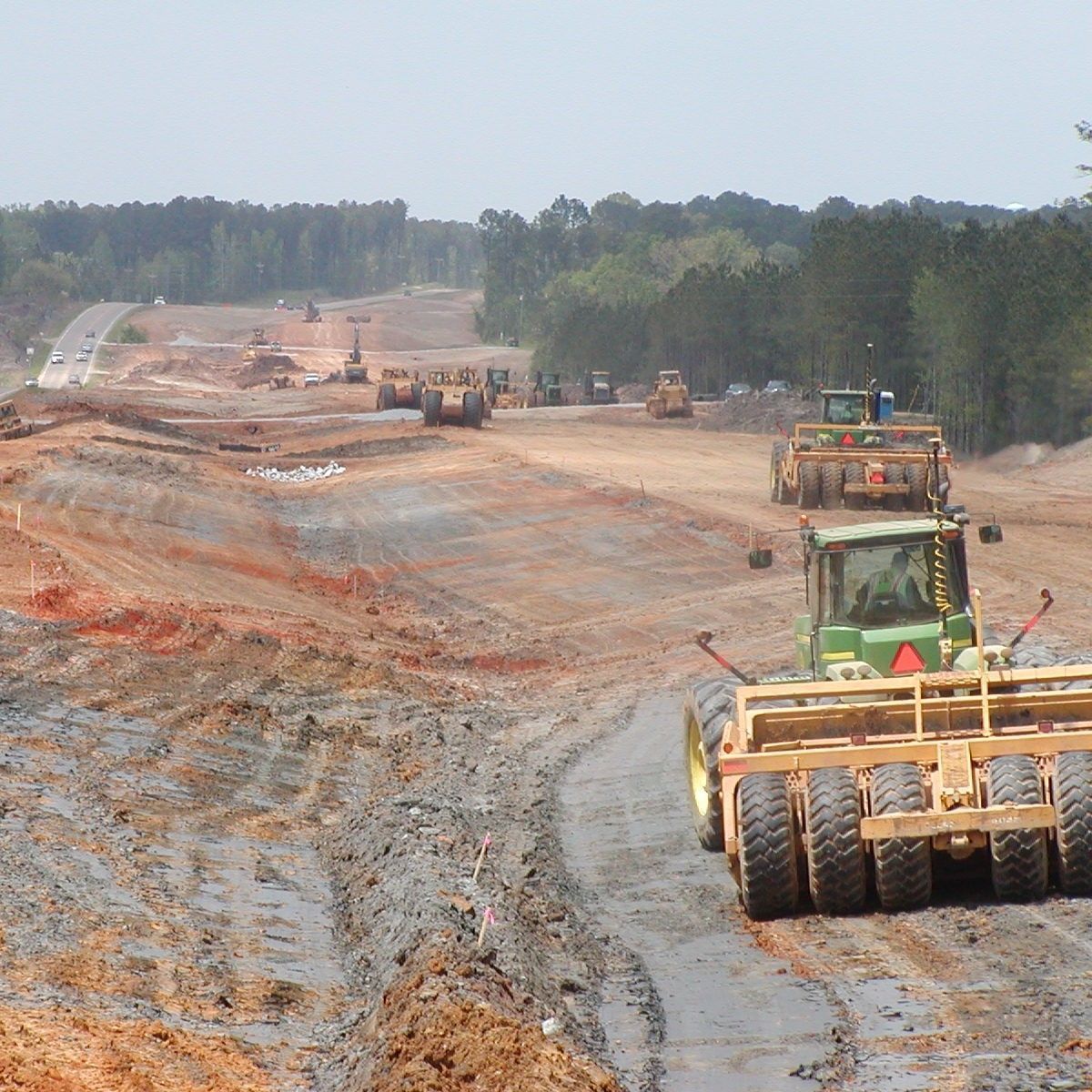 A tractor with a yellow trailer is driving down a dirt road