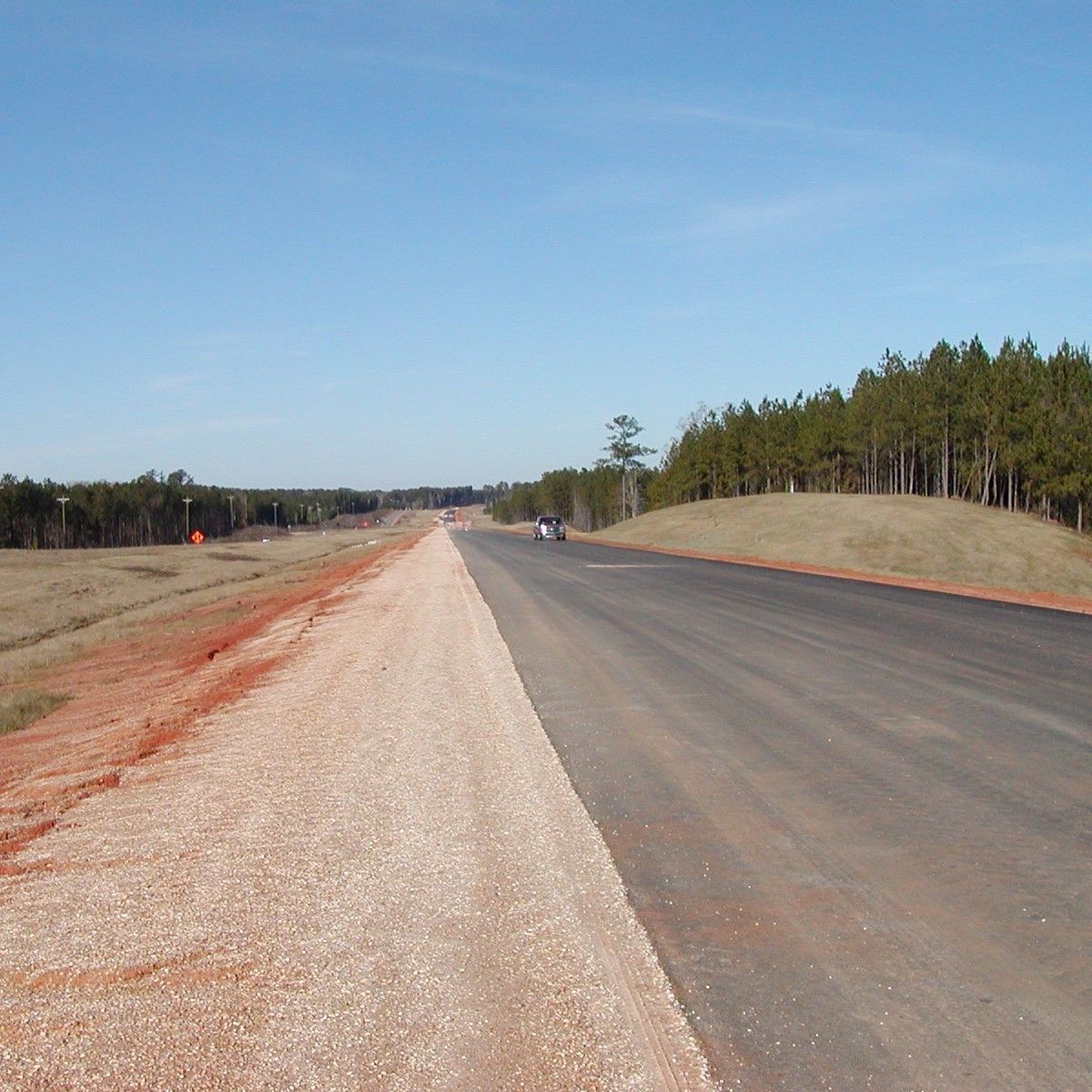 A road with gravel on the side and trees on the other side