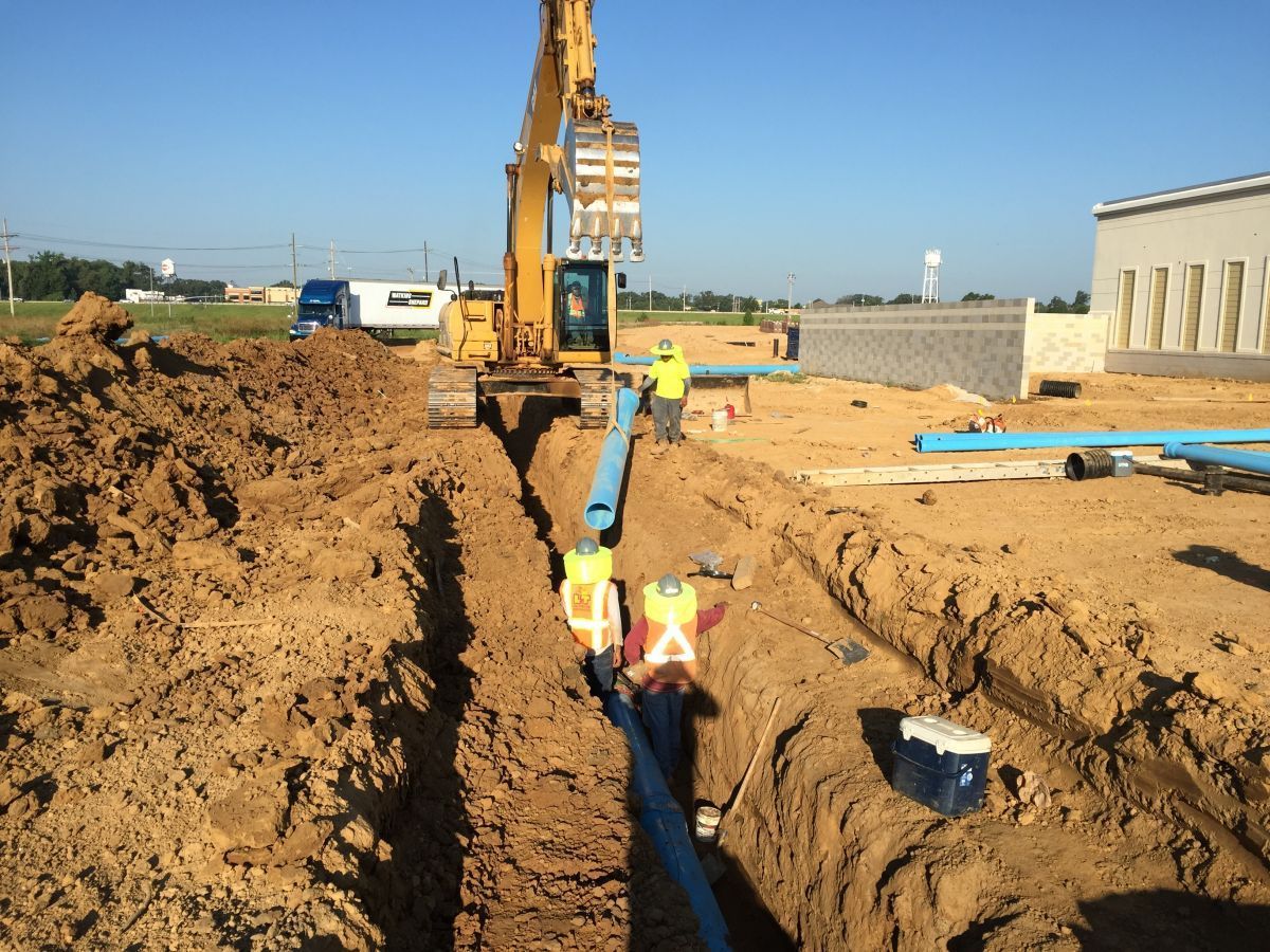 A yellow excavator is digging a trench in the dirt