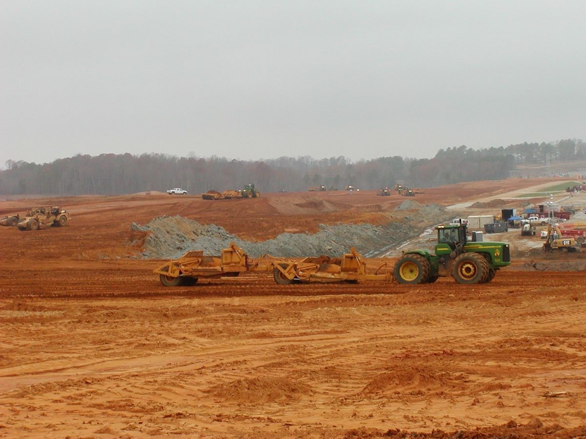 A green tractor is driving through a dirt field.